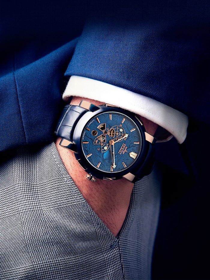 Automatic watch "Meteorit" in blue on the wrist of a gentleman wearing a blue suit and gray trousers.